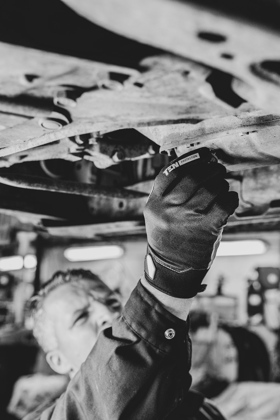 A mechanic is working under a car with Ten Protection work gloves on.